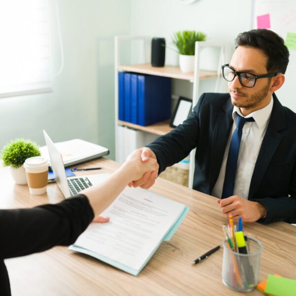 Business partner in a suit shaking hands with a caucasian professional colleague. Blond woman signing a deal and contract with a lawyer in a corporate office